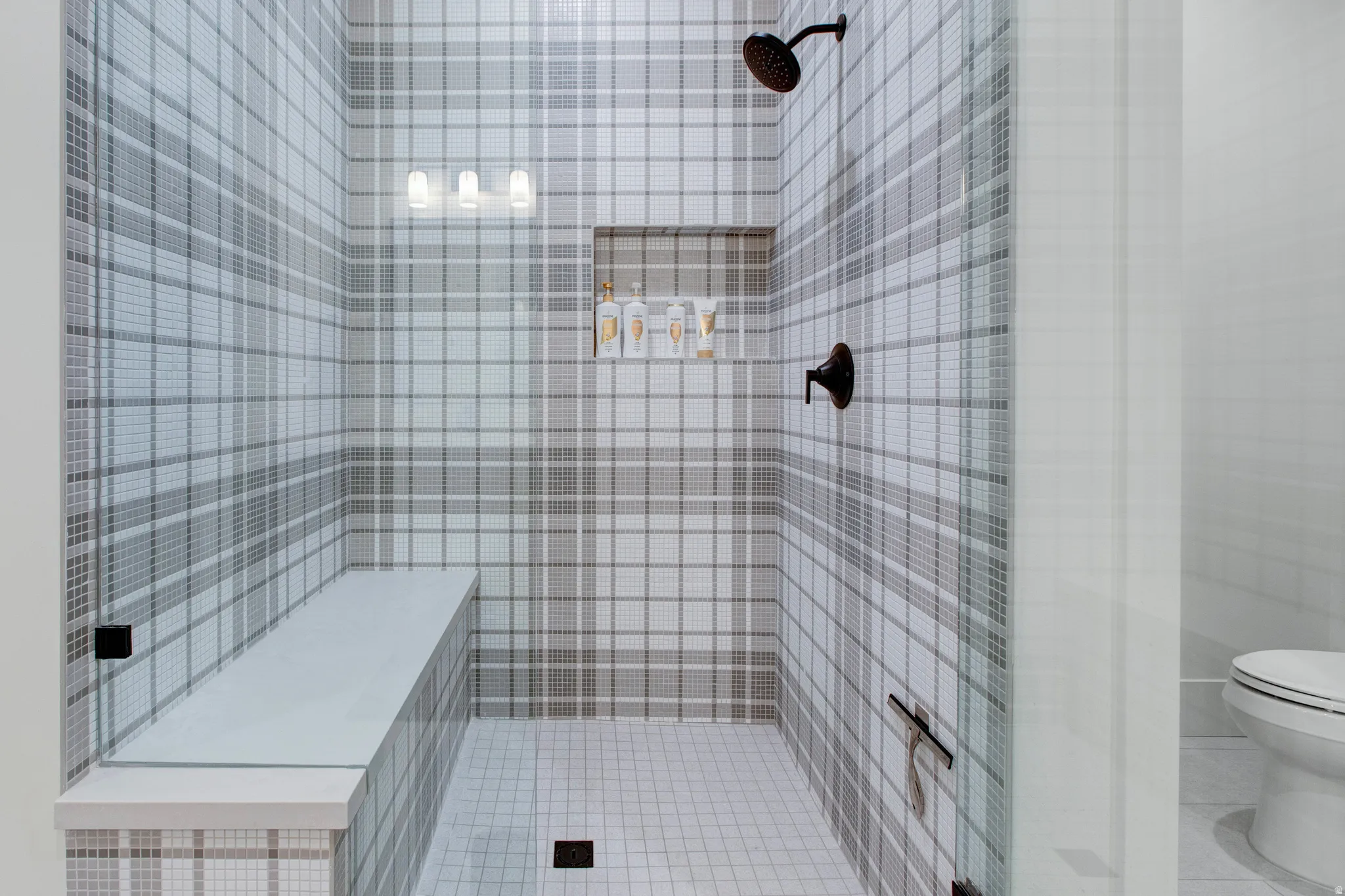 Walk-in shower with plaid-patterned mosaic tile walls, a built-in bench, and clear glass enclosure