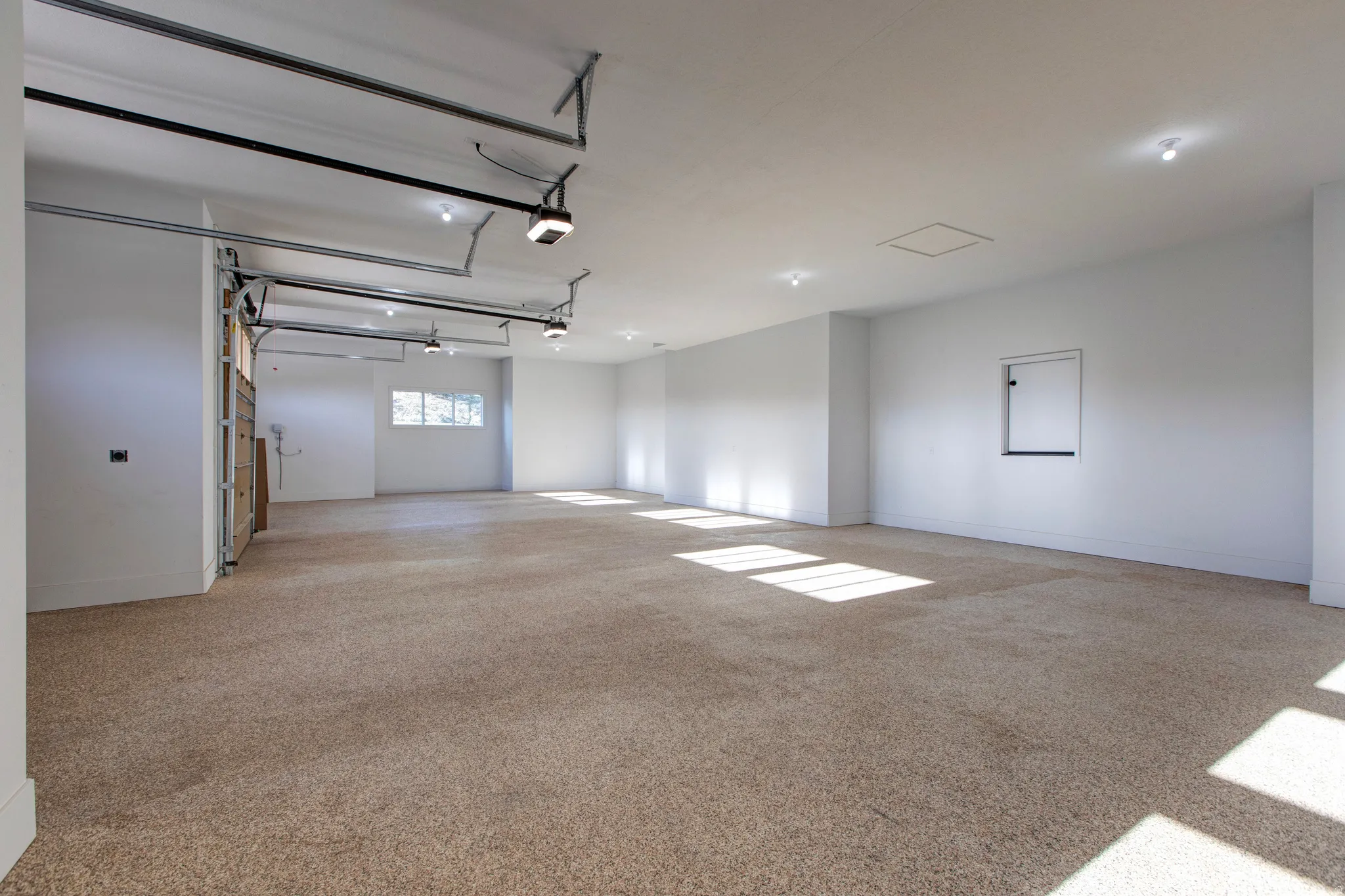 Spacious garage featuring light brown carpet flooring, multiple windows, recessed lighting, and white walls