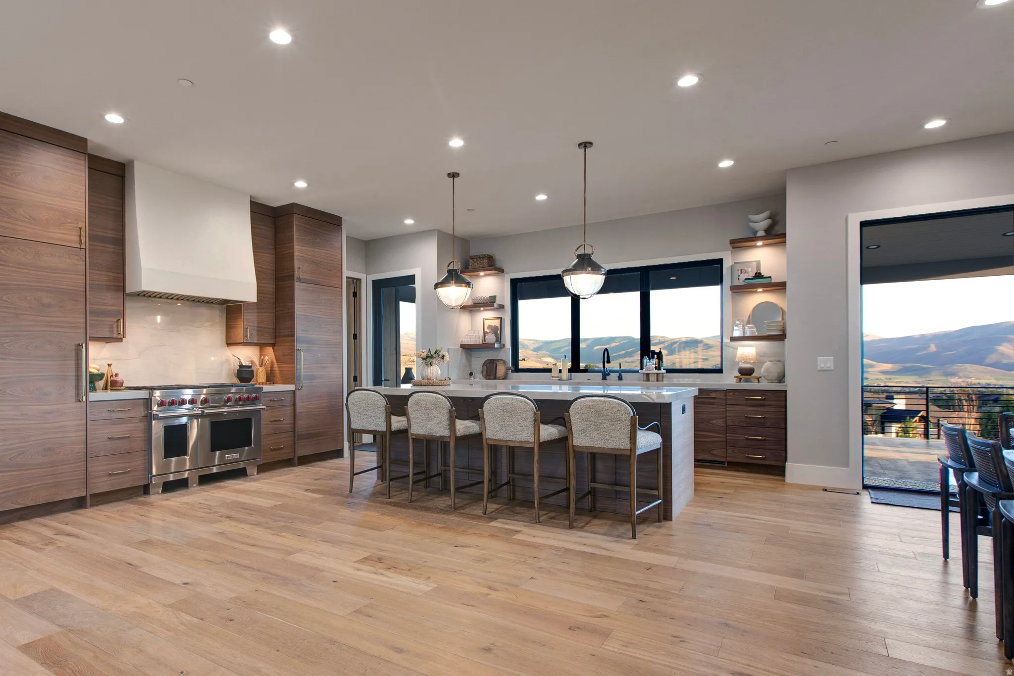 Gourmet kitchen with wood-finish flooring, a substantial island featuring a light-toned countertop, stainless steel appliances, and dark-framed windows overlooking distant mountains