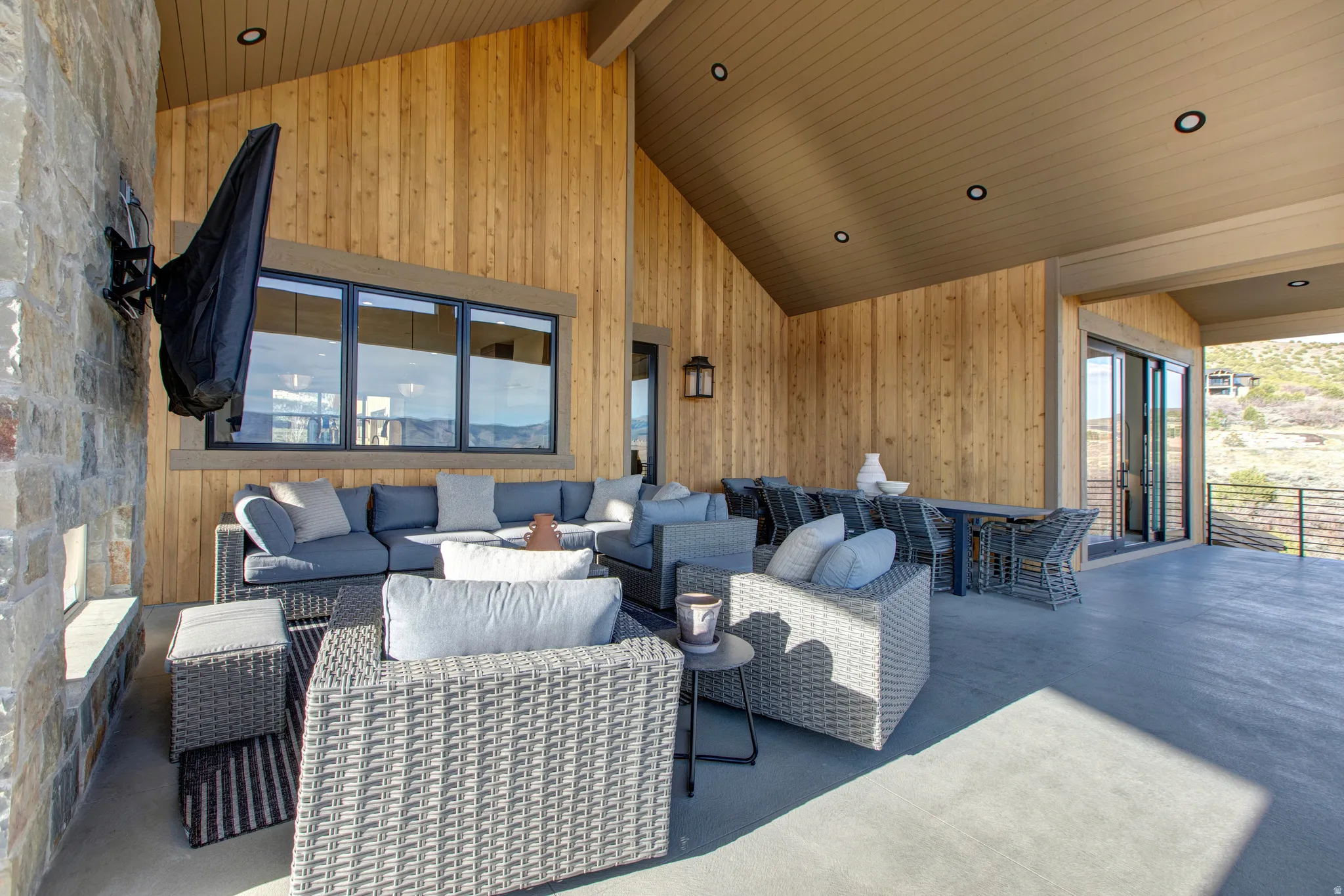 Expansive covered patio featuring a stone accent wall, wood-paneled siding, and a vaulted ceiling with recessed lighting
