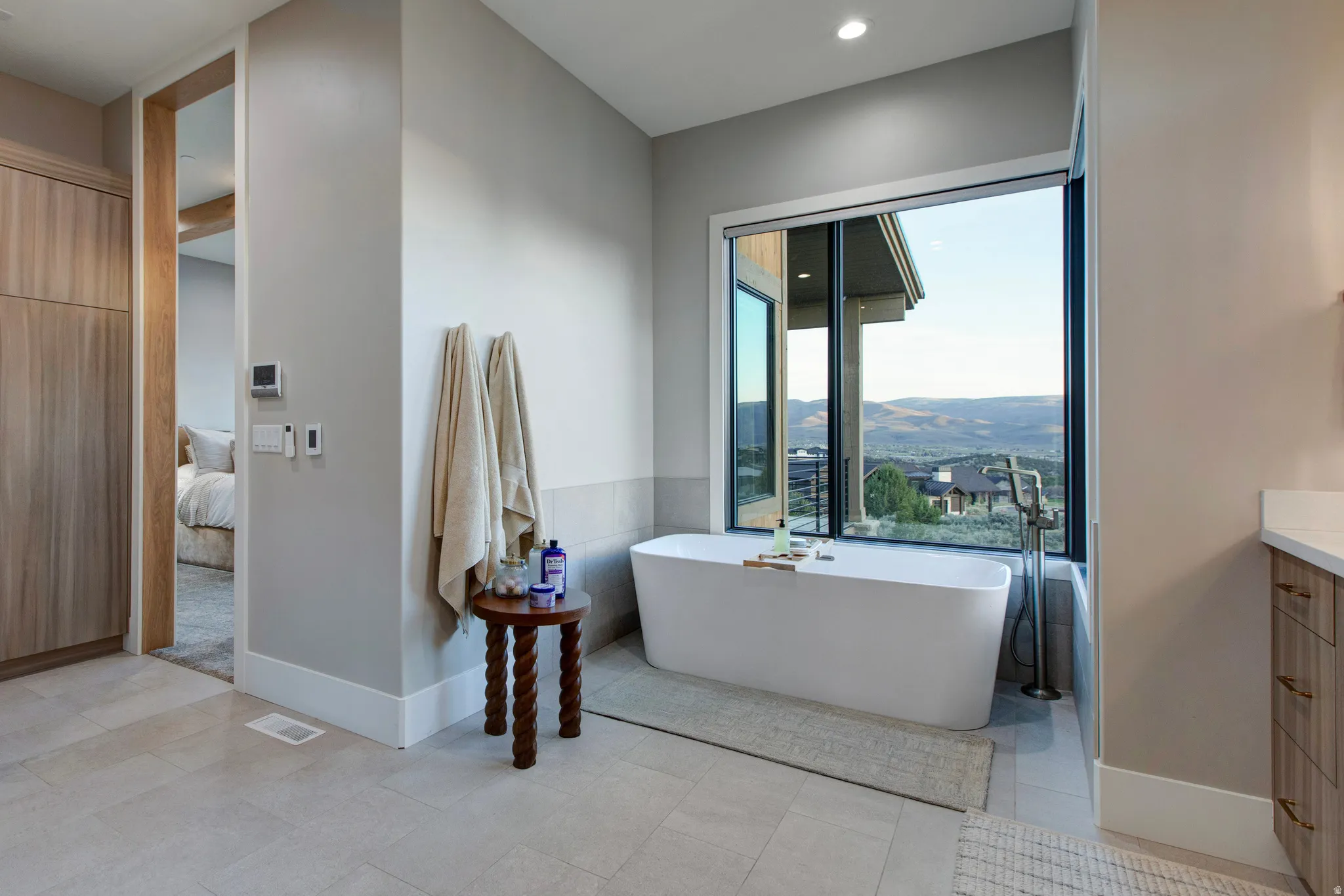 Freestanding soaking tub with a floor-mounted fixture, set against a large window revealing a mountain landscape
