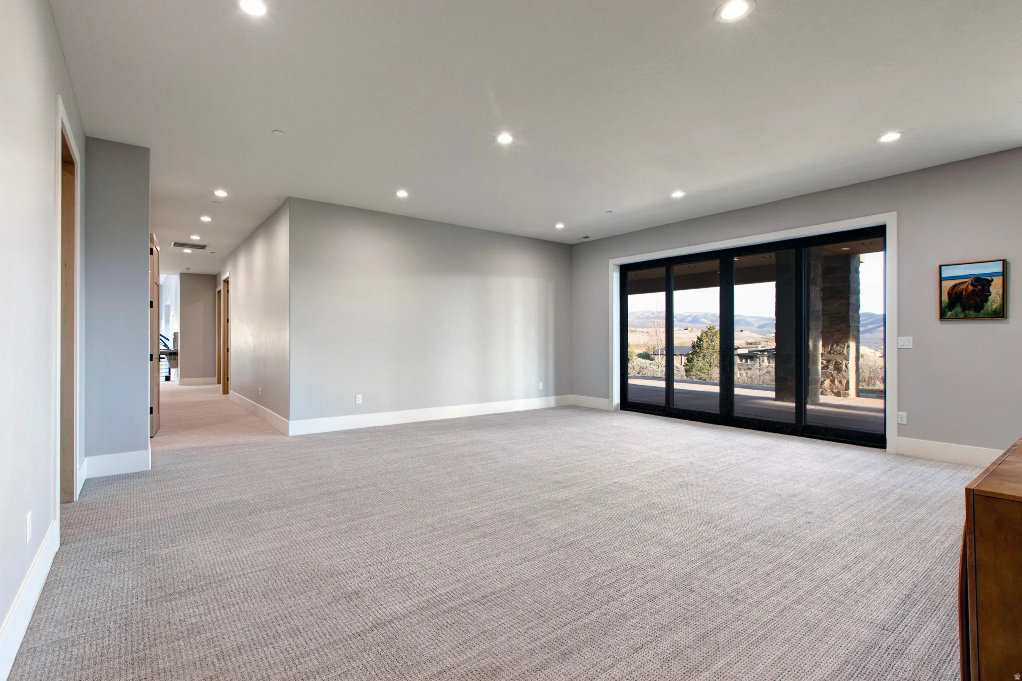 Spacious interior room with light gray walls, recessed lighting, and light gray patterned carpeting