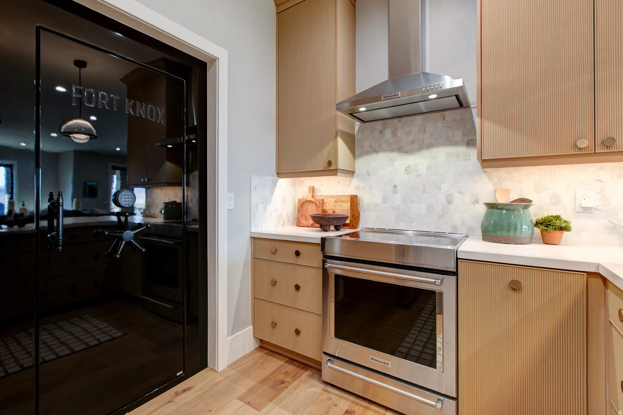 Kitchen area featuring wood-finish flooring, light-toned cabinetry, stainless steel range and hood, light-colored countertops, and a patterned tile backsplash