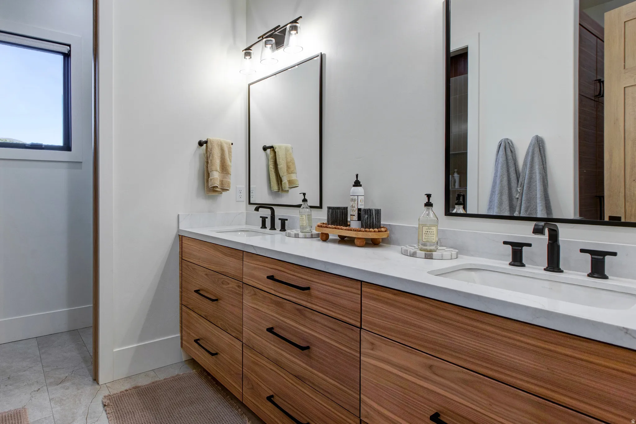 Double vanity featuring wood-finish cabinetry, white stone countertops, and matte black fixtures