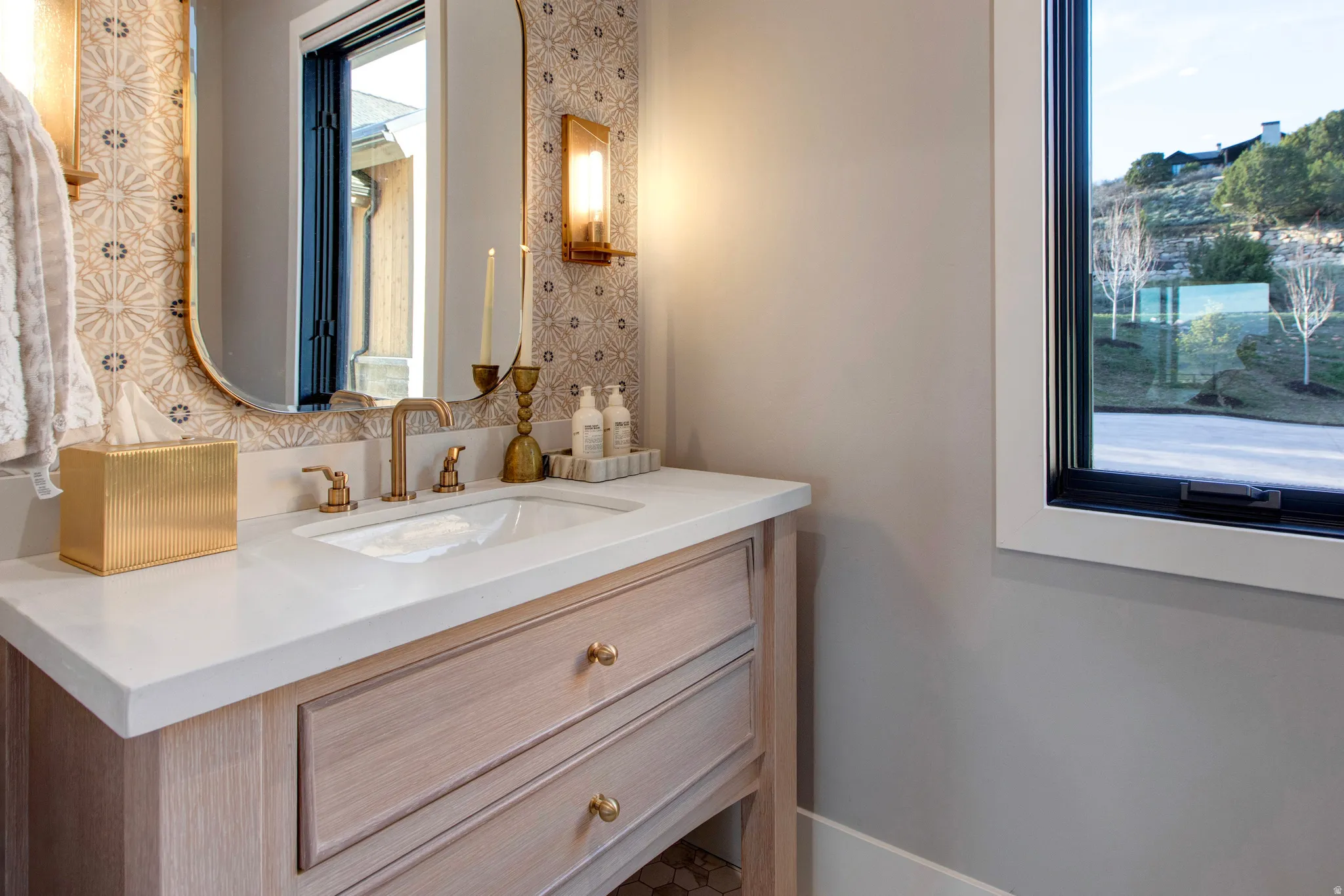 Vanity featuring a light wood-finish cabinet with brass hardware, a white countertop, and an undermount sink with brass fixtures