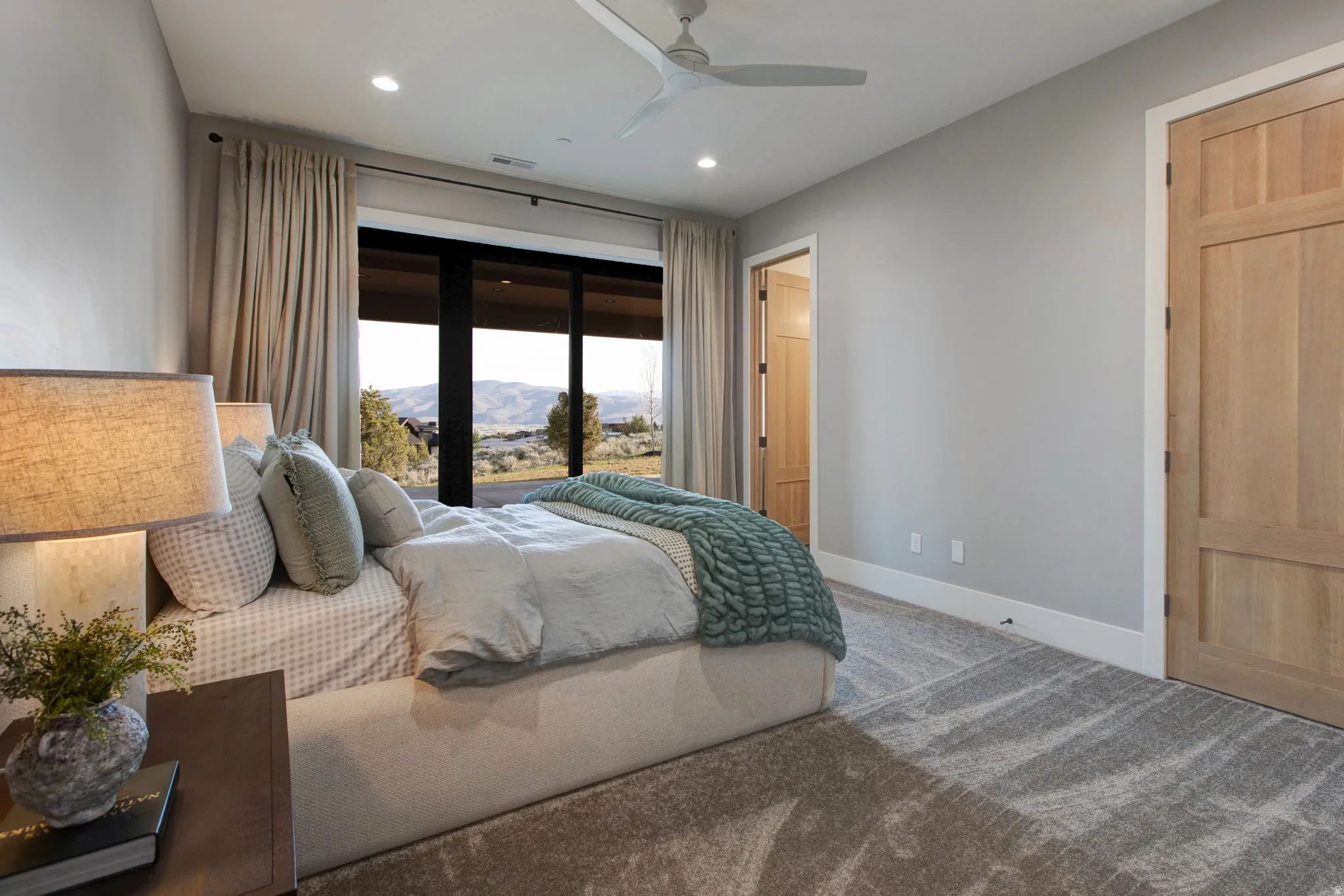 Wall-to-wall carpeting with a light gray pattern, expansive window framing distant mountains, recessed lighting, ceiling fan, and natural wood-finish interior doors