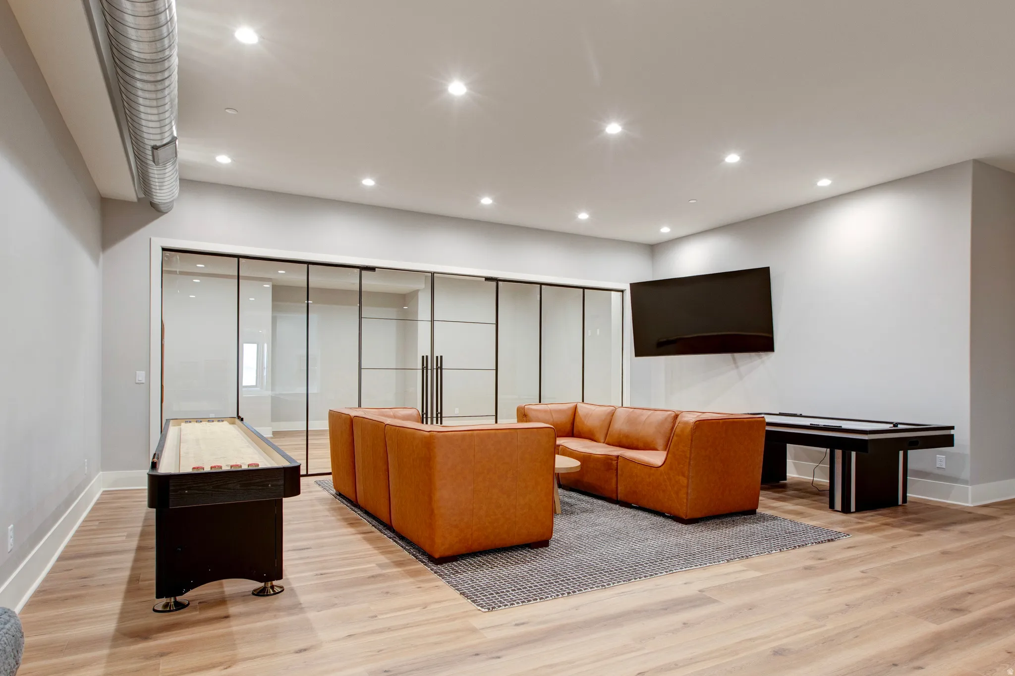 Spacious entertainment area featuring light wood-finish flooring, recessed lighting, and exposed ductwork
