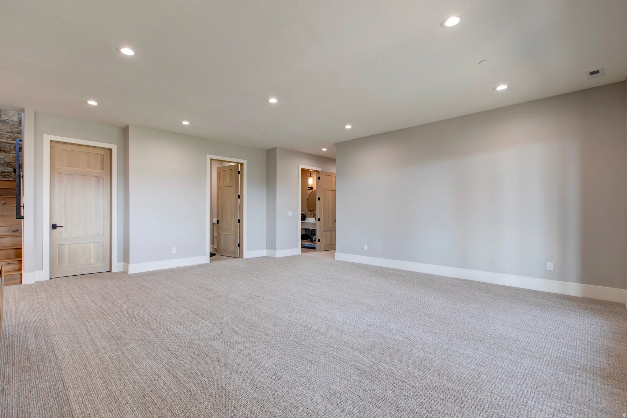 Spacious room featuring light-colored carpeting, recessed lighting, and light wood-paneled doors with black hardware