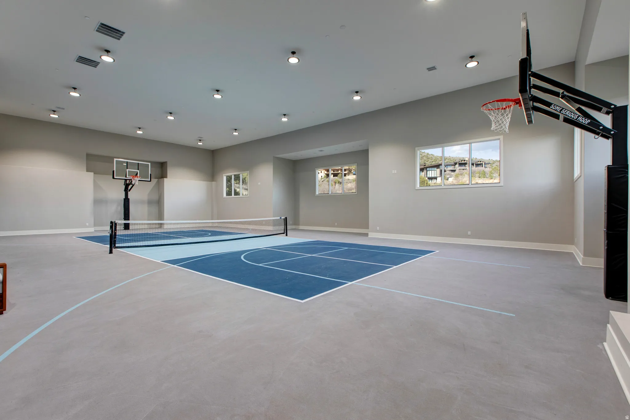 Indoor multi-sport court featuring light gray walls, recessed lighting, and multiple windows