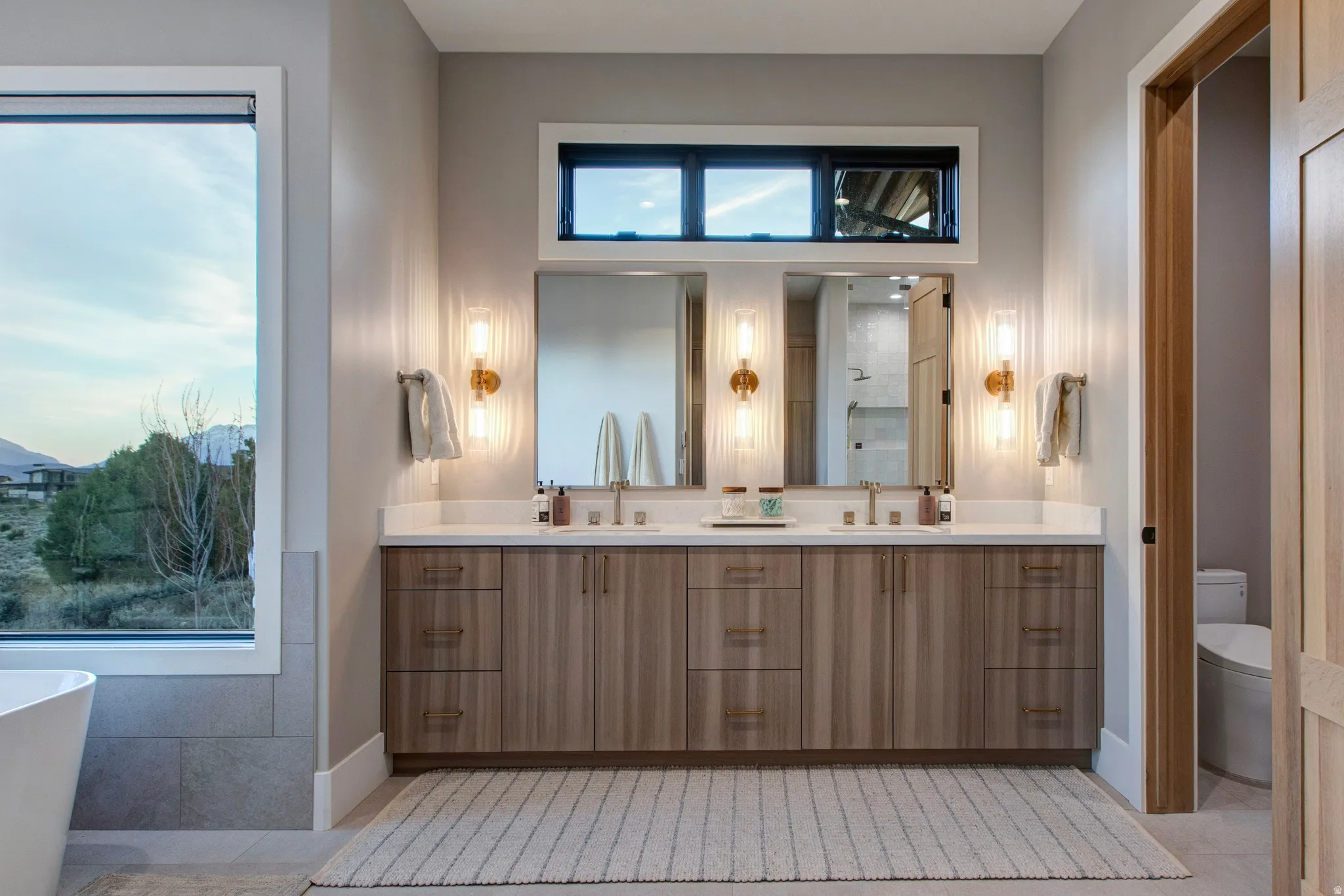 Expansive double vanity with wood-finish cabinetry, dual undermount sinks, and a light-toned countertop