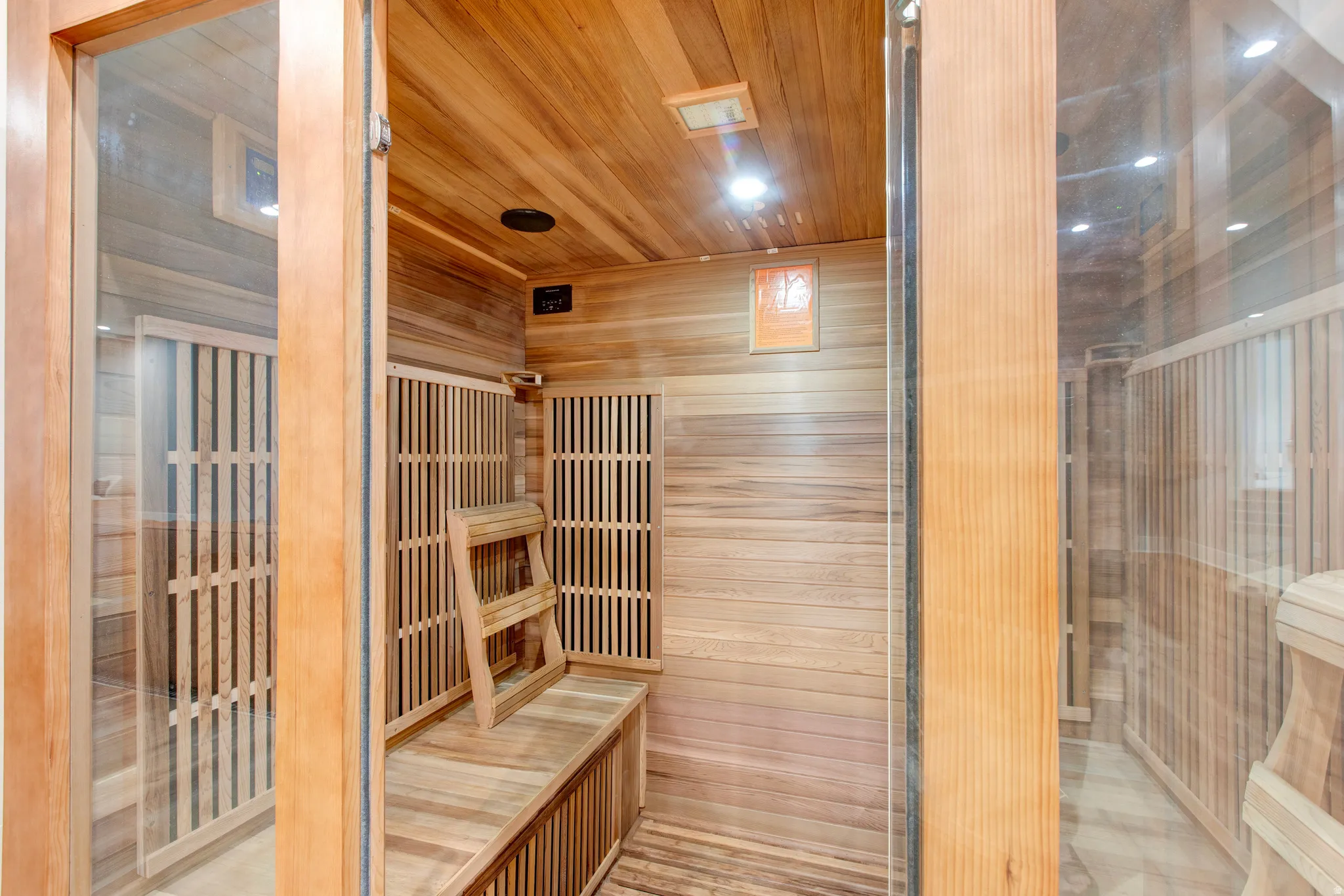 Dedicated sauna featuring natural wood paneling, built-in wooden benches, and clear glass entry doors