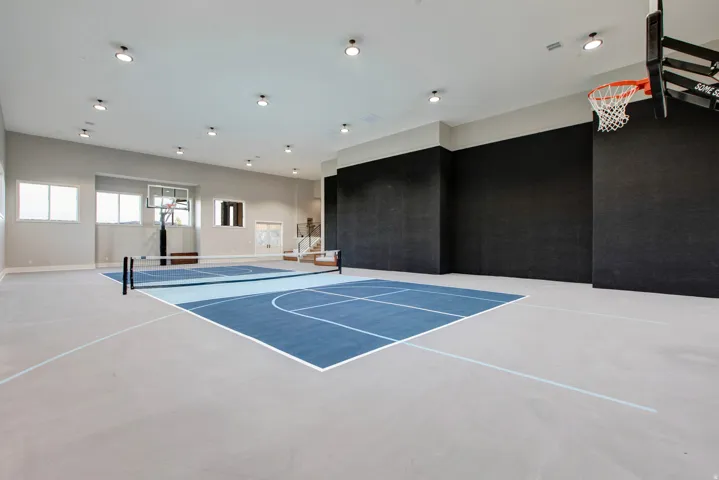 Indoor athletic court featuring a basketball hoop, a net for court sports, and perimeter striping on a light gray and blue surface