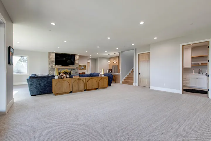 Expansive carpeted living area featuring recessed lighting, a stone-clad fireplace, and a built-in entertainment center