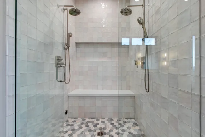 Glass-enclosed shower featuring dual shower heads, a built-in bench, a recessed niche, and hexagonal floor tiling