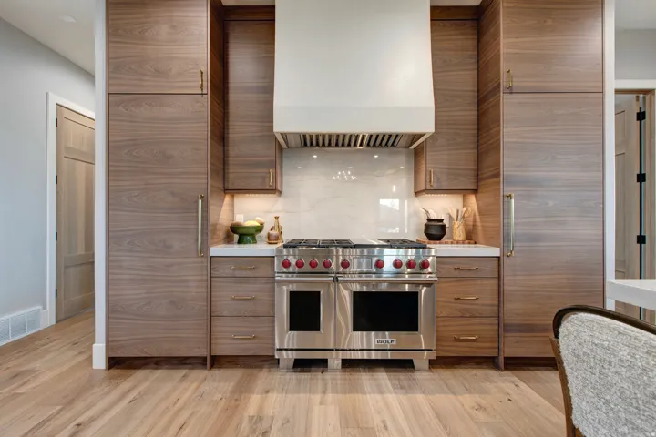 Gourmet kitchen featuring a stainless steel range with red knob accents, a white vent hood, integrated wood-finish cabinetry, a white countertop, and a light-colored backsplash