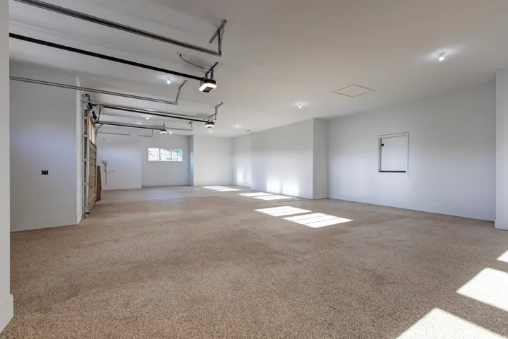 Spacious garage featuring light brown carpet flooring, multiple windows, recessed lighting, and white walls