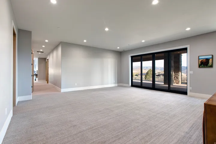 Spacious interior room with light gray walls, recessed lighting, and light gray patterned carpeting