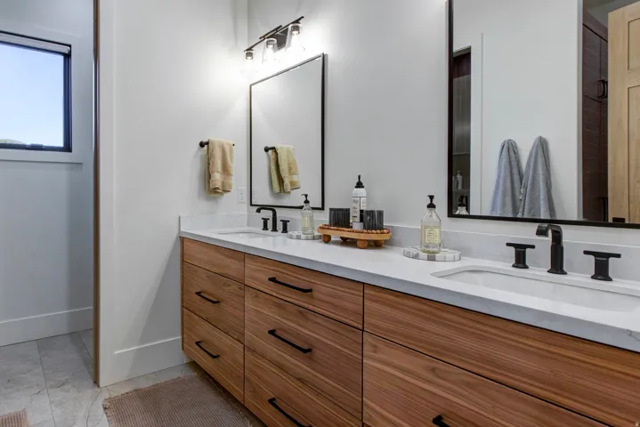 Double vanity featuring wood-finish cabinetry, white stone countertops, and matte black fixtures