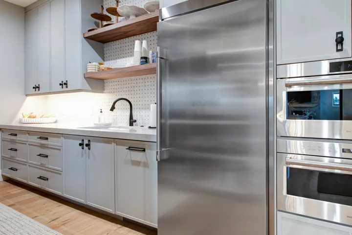 Gourmet kitchen featuring a built-in stainless steel refrigerator, double wall ovens, a large sink with a matte black faucet, light grey cabinetry with black hardware, and wood-finish flooring