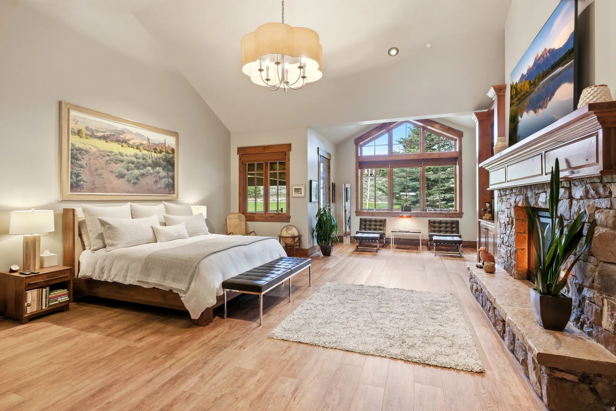 Vaulted ceiling with a central chandelier, wood-finish flooring, and a stone-clad fireplace with a mantle