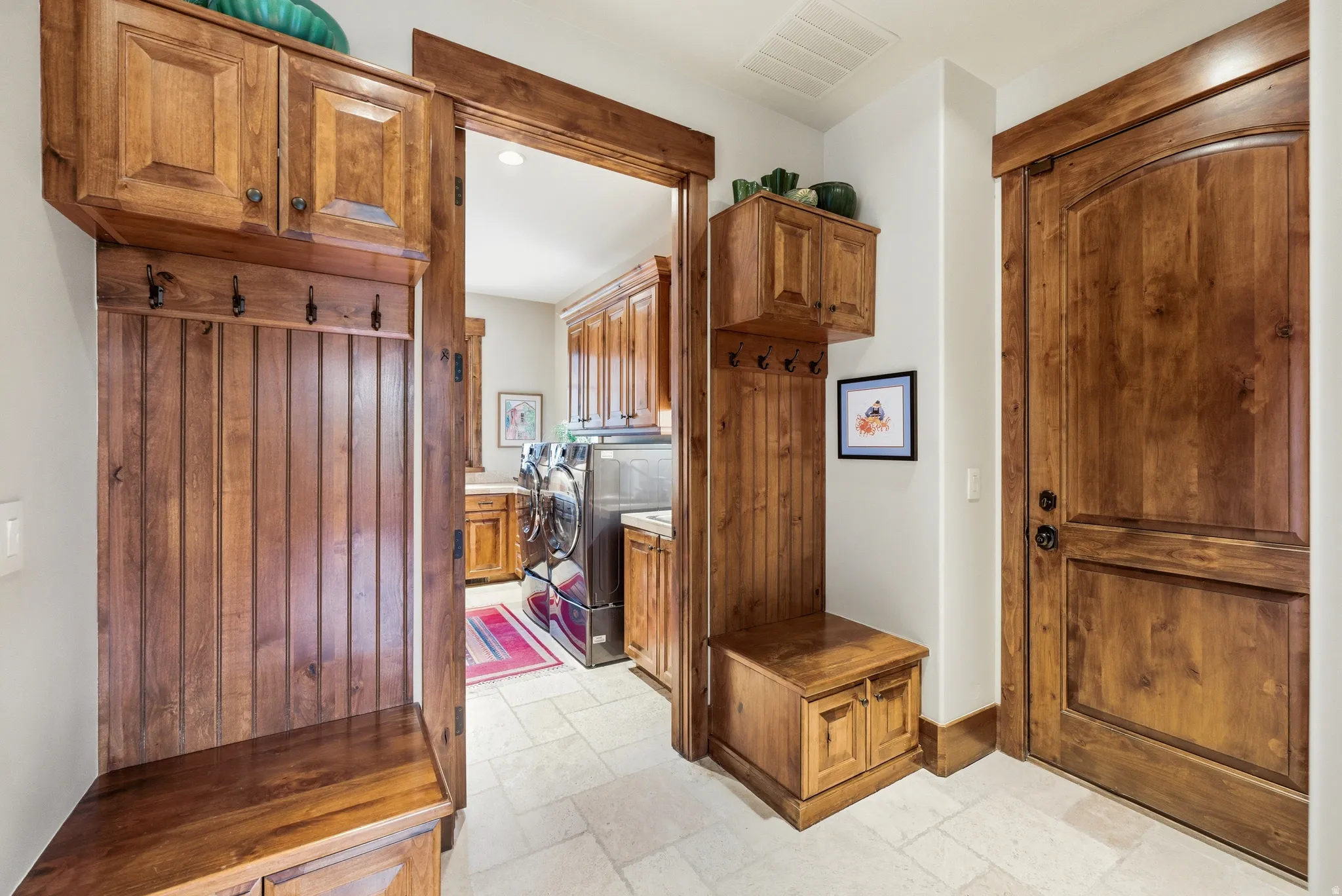 Entryway featuring wood-finish mudroom-style built-ins with hooks and storage, light-toned tile flooring, and a solid wood-finish door with a dark handle