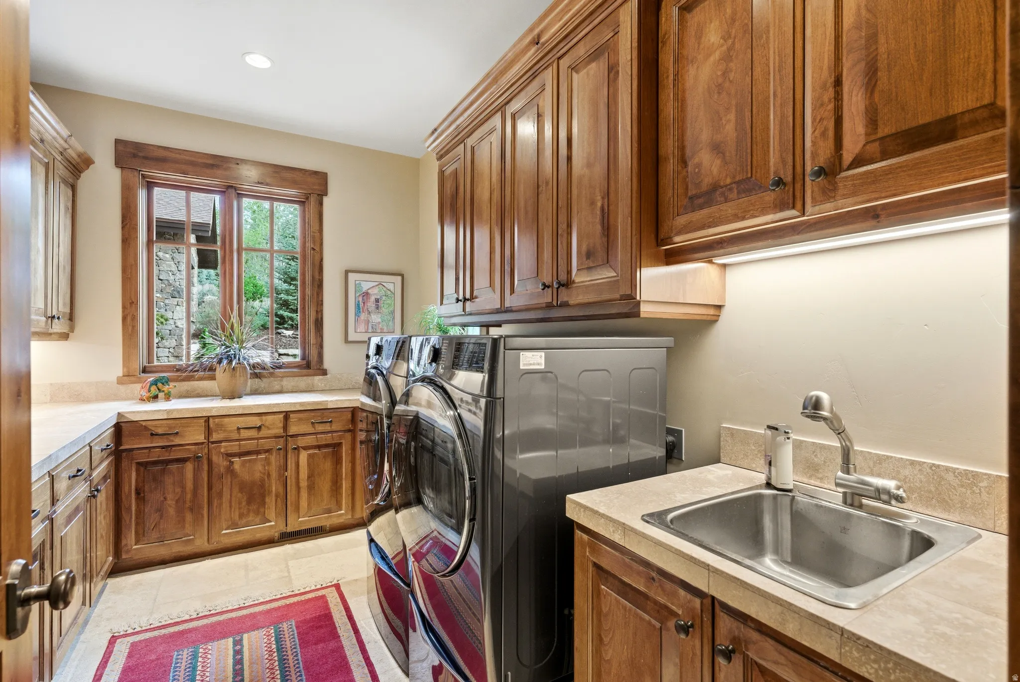 Laundry room featuring extensive wood cabinetry, tile flooring, stone-look countertops, and a utility sink