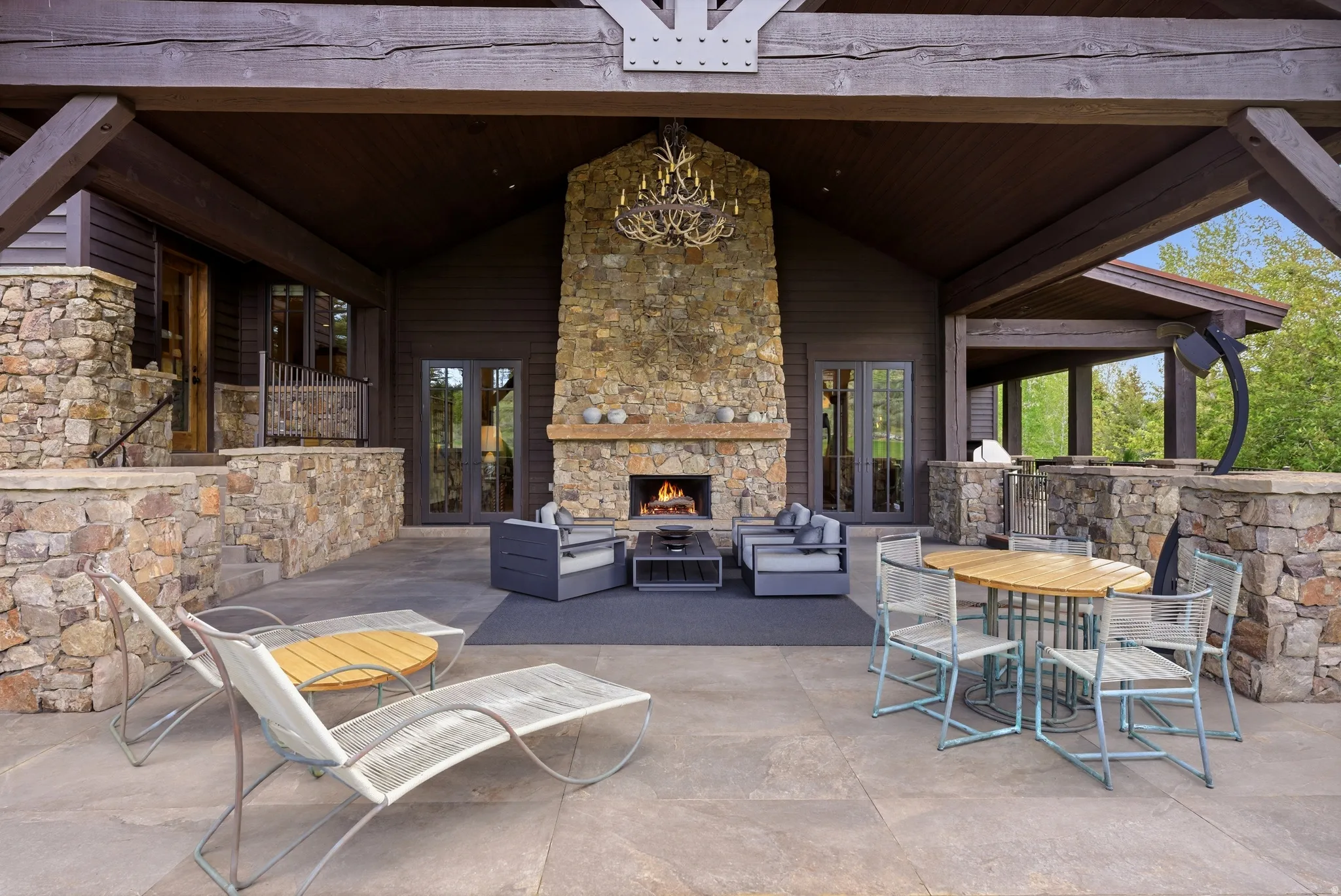 Expansive outdoor living area featuring a stone fireplace, wood beam ceiling, and a large stone patio