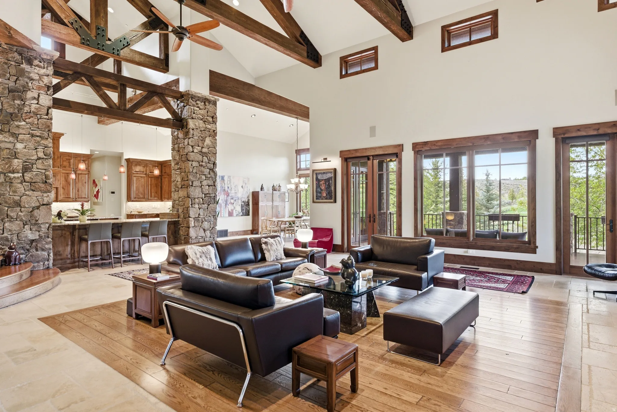 Spacious living area featuring exposed wood beam ceilings, stone-clad architectural columns, and wood-finish flooring