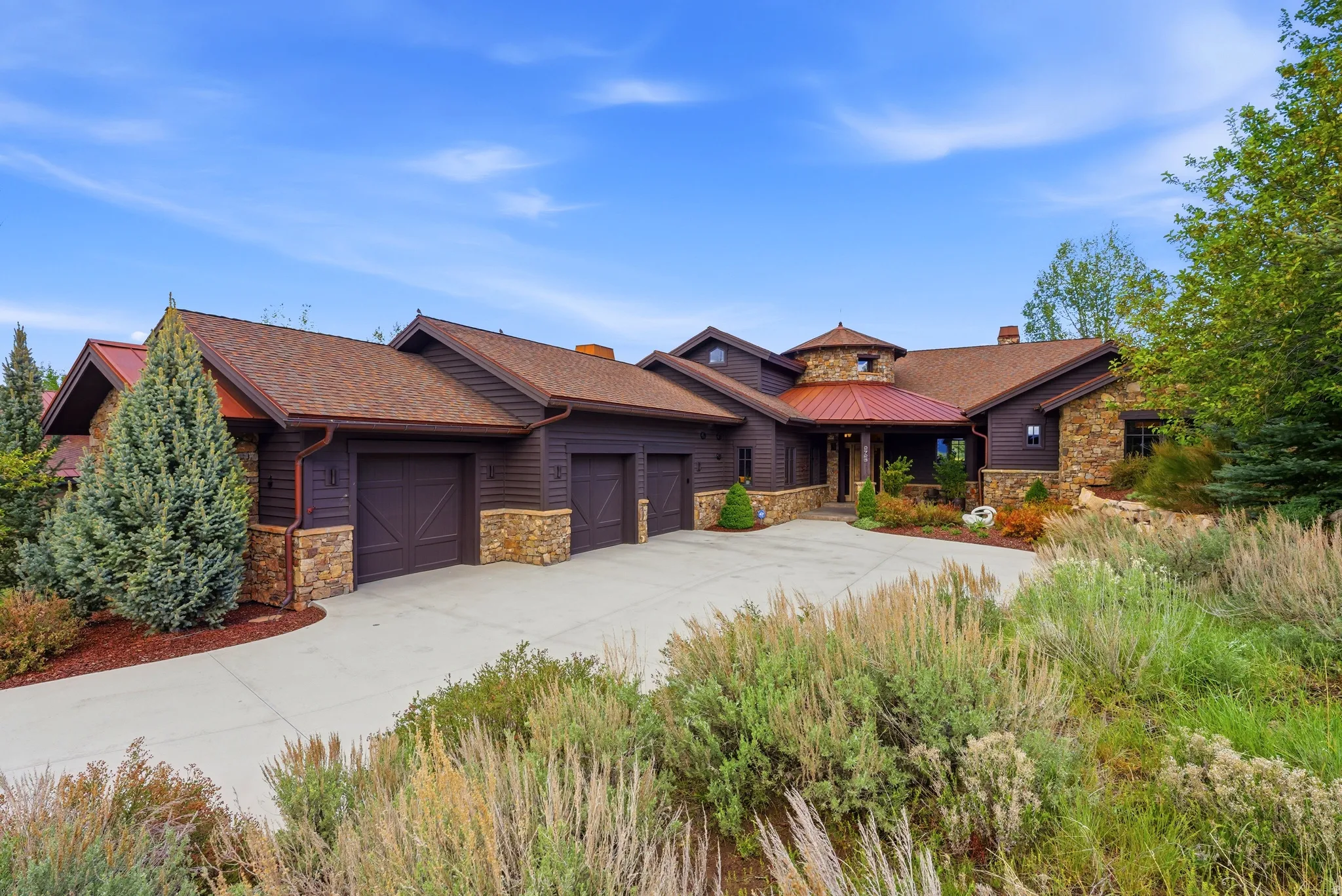 Contemporary home with a multi-car garage, stone and wood-paneled exterior, red metal roof accents, and a winding concrete driveway