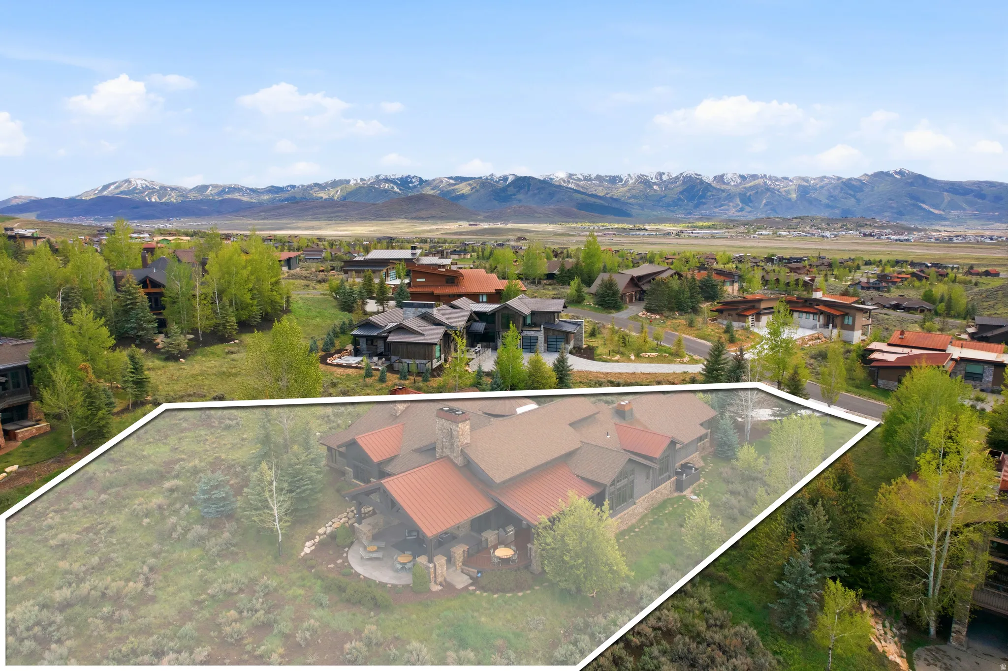 Spacious property with a large residence featuring a red metal roof and stone chimney, set against a backdrop of distant mountains