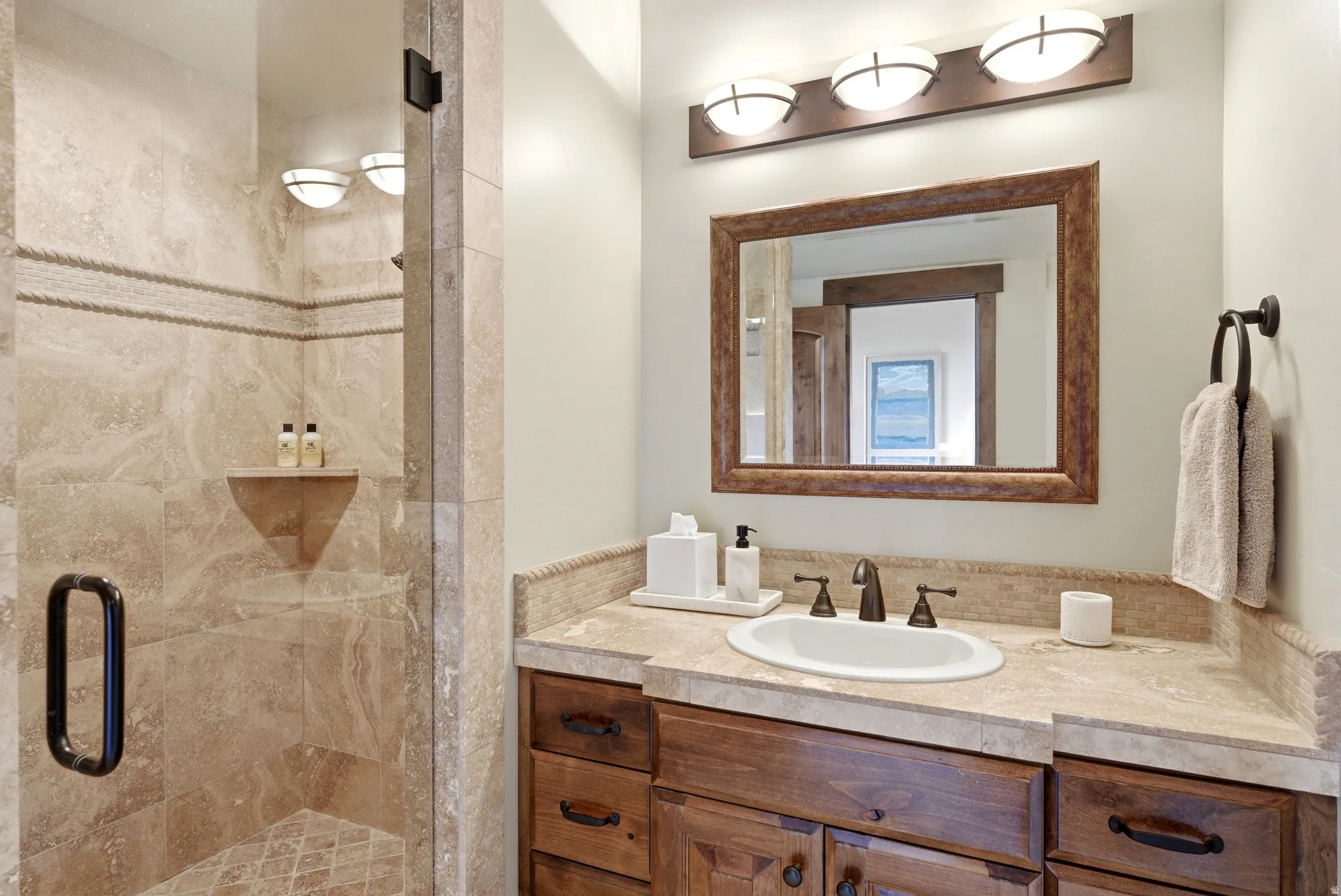 Bathroom featuring a glass-enclosed shower with full-height stone tile, a built-in shower niche, and a contrasting decorative tile band