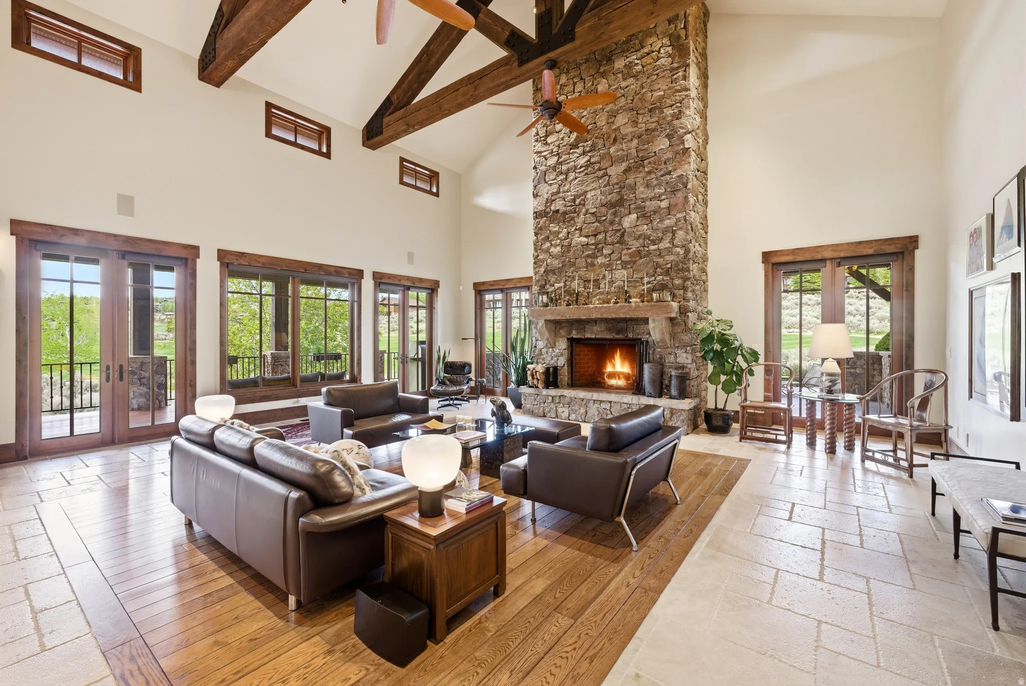 Grand living area featuring a floor-to-ceiling stone fireplace, vaulted ceiling with exposed wood beams, and a dual-tone flooring with wood planks and stone tile