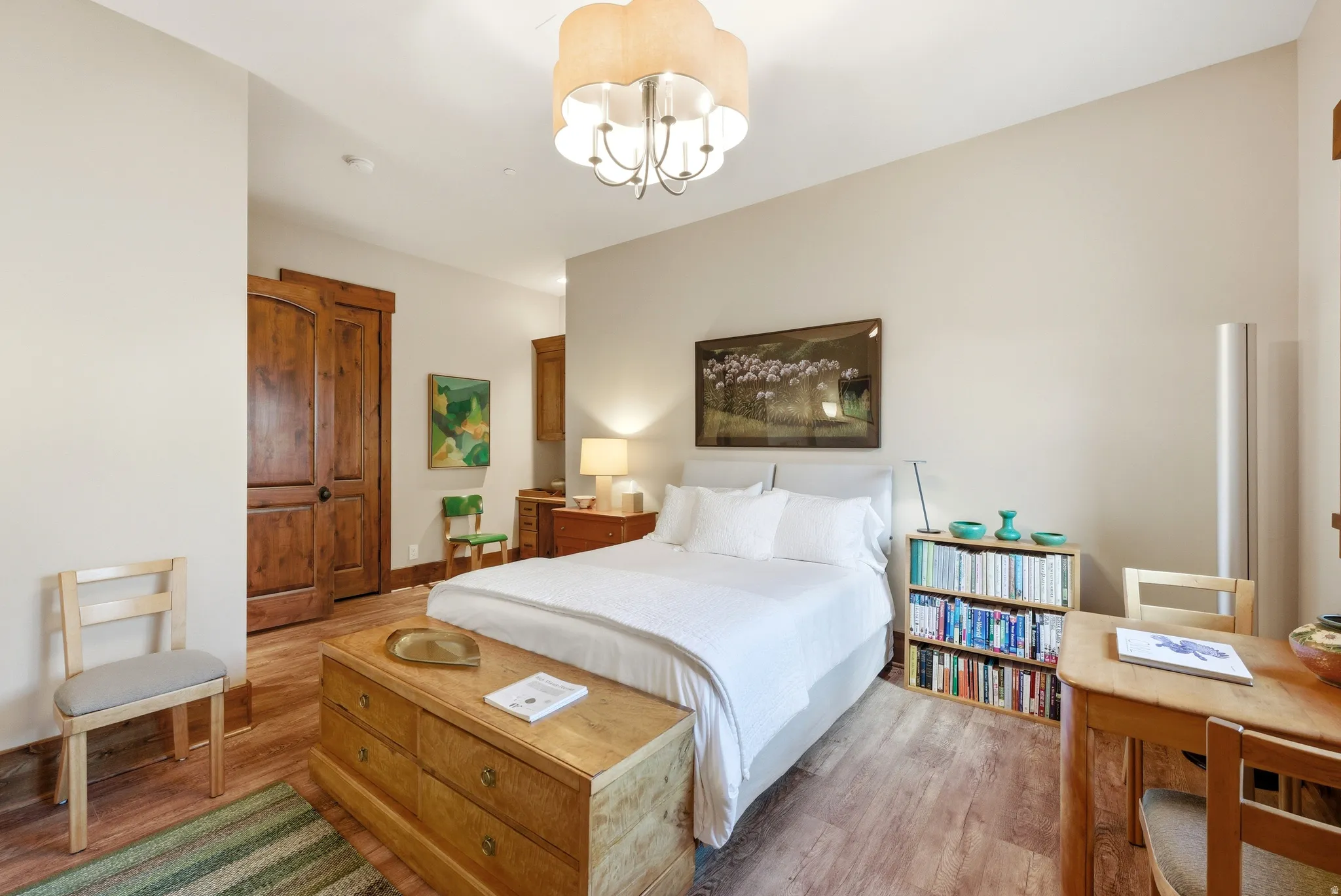 Bedroom featuring wood-finish flooring, a contemporary chandelier, two panel wood doors, and light-toned walls