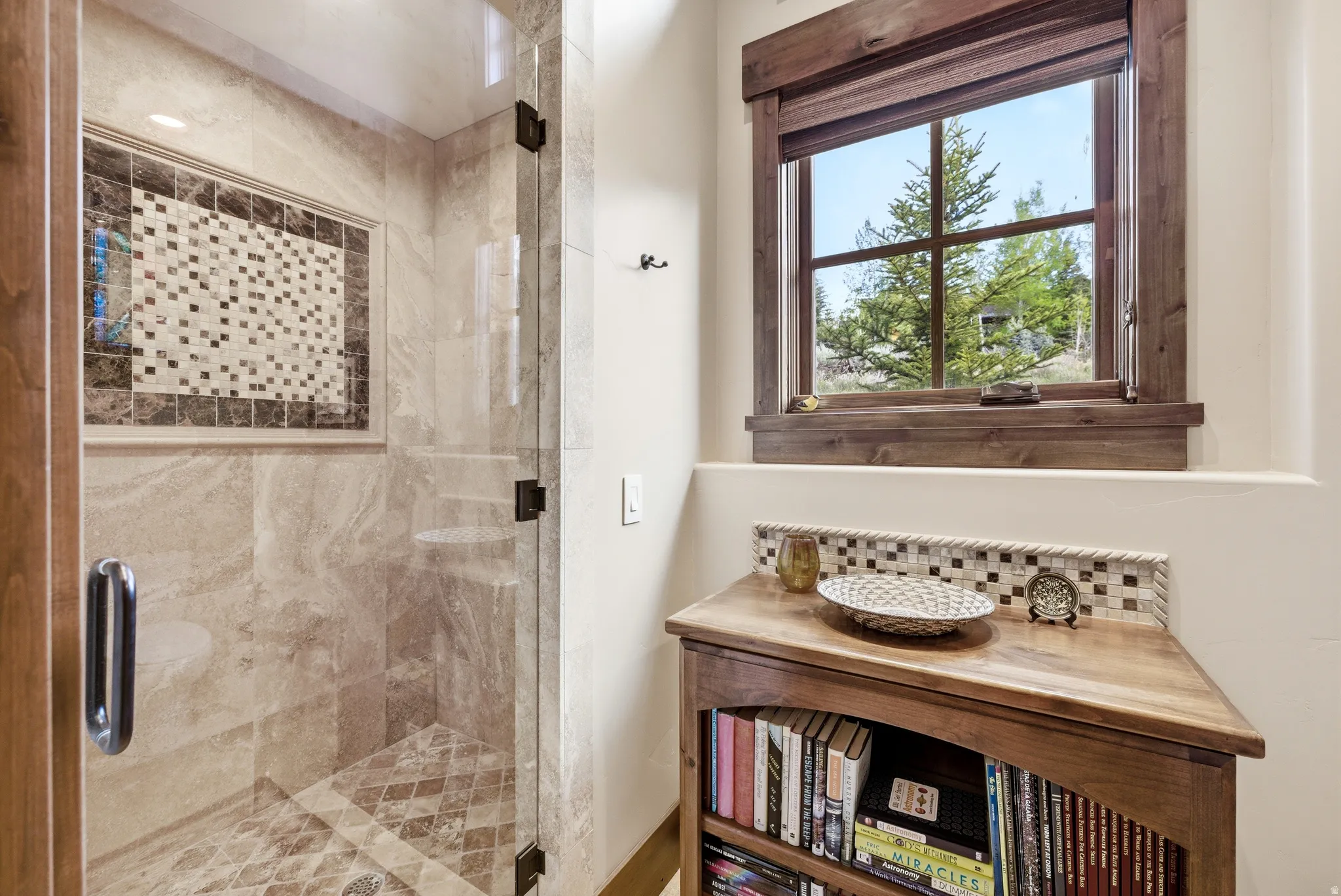 Glass-enclosed shower with stone tile walls, decorative mosaic inlay, and patterned tile flooring