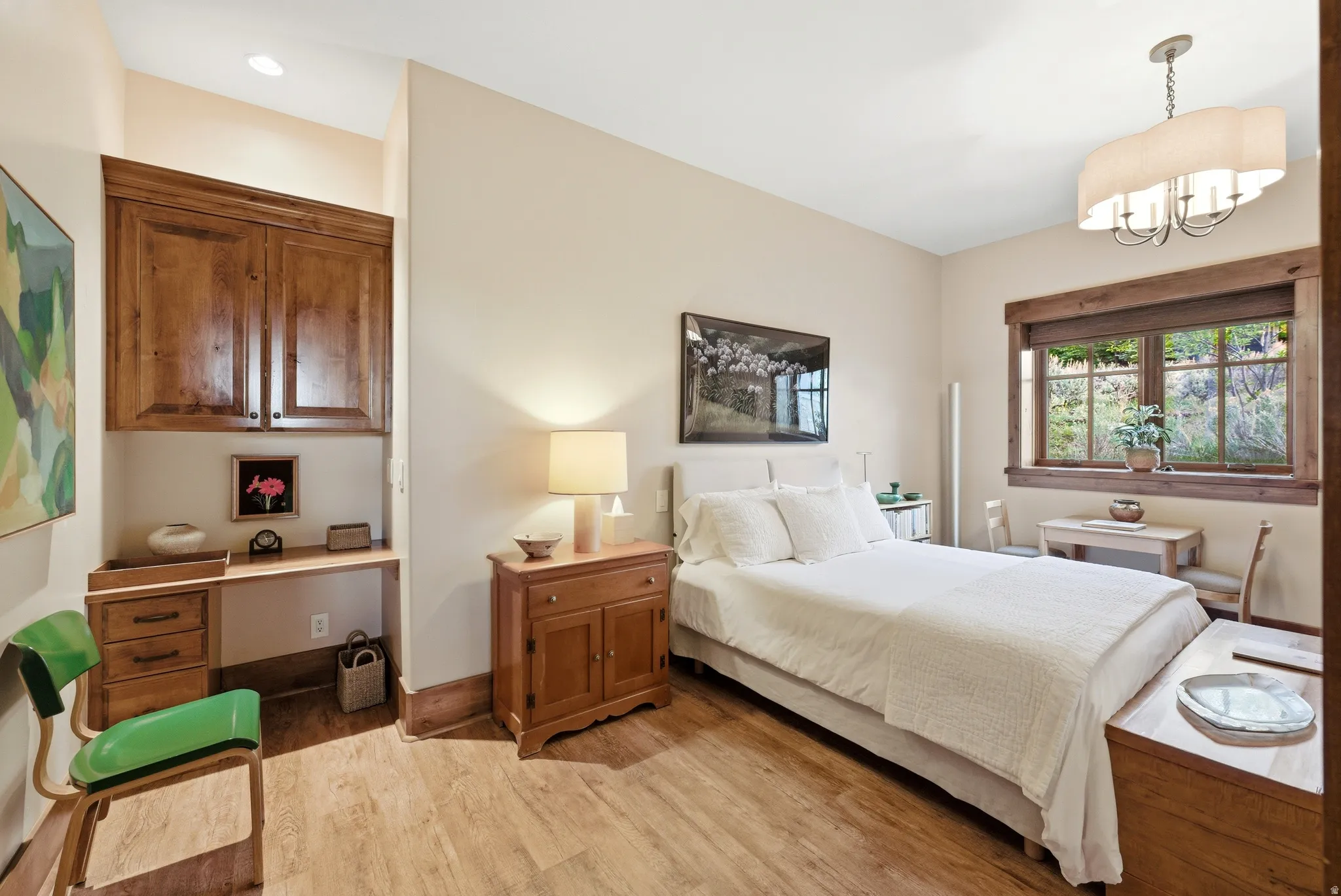 Bedroom featuring wood-finish flooring, a built-in desk with overhead cabinetry, a wood-trimmed window, and a decorative ceiling light fixture