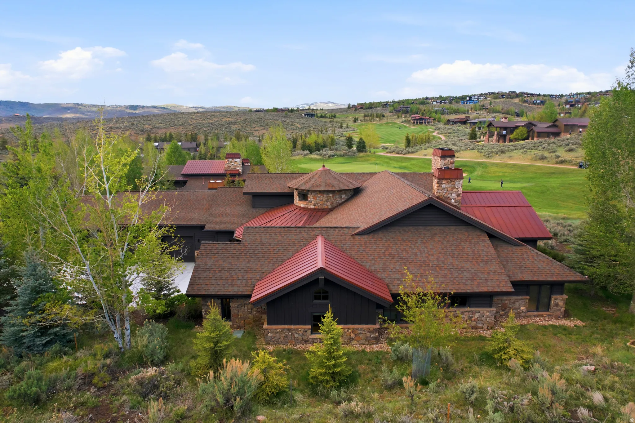 Expansive residence featuring a stone and dark siding exterior with multiple pitched roofs