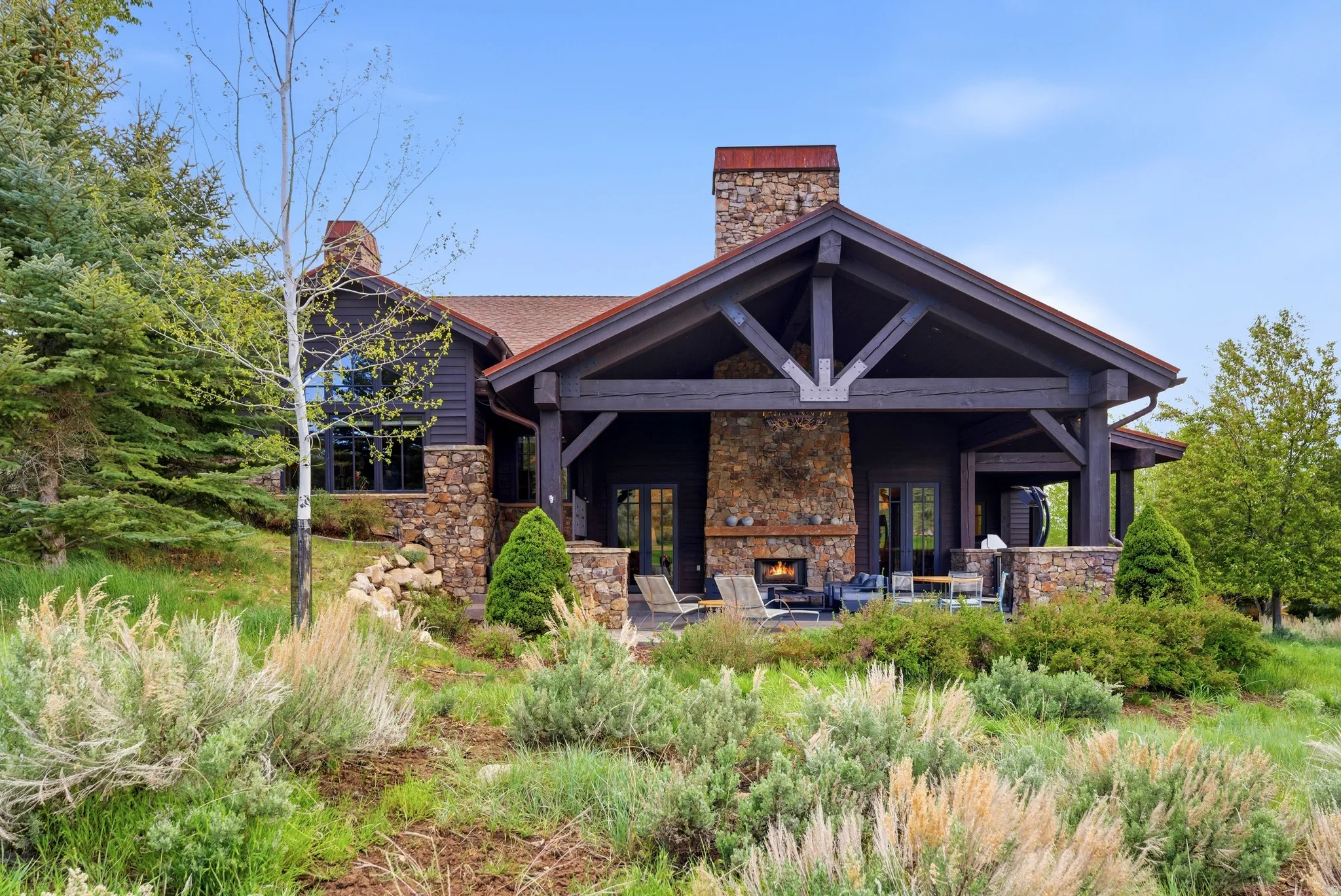 Stone and timber frame lodge-style home featuring a covered patio with an outdoor fireplace