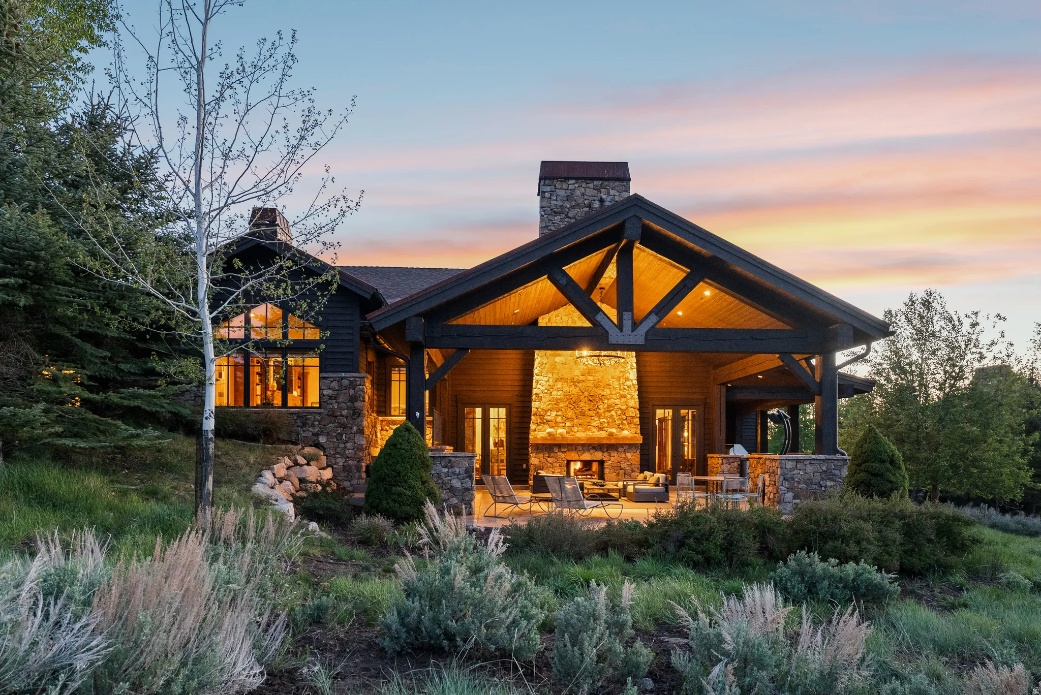 Expansive outdoor living area featuring a stone fireplace, wood-beamed ceiling, and a covered patio