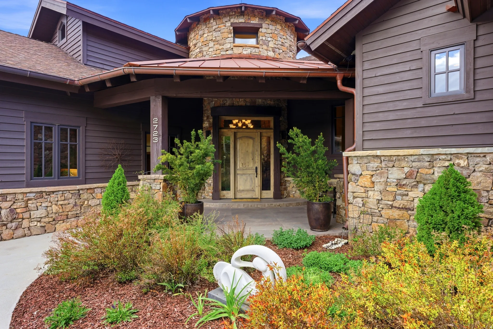 Stone and siding exterior featuring a prominent circular turret, a decorative wood entry door, and copper-toned gutters