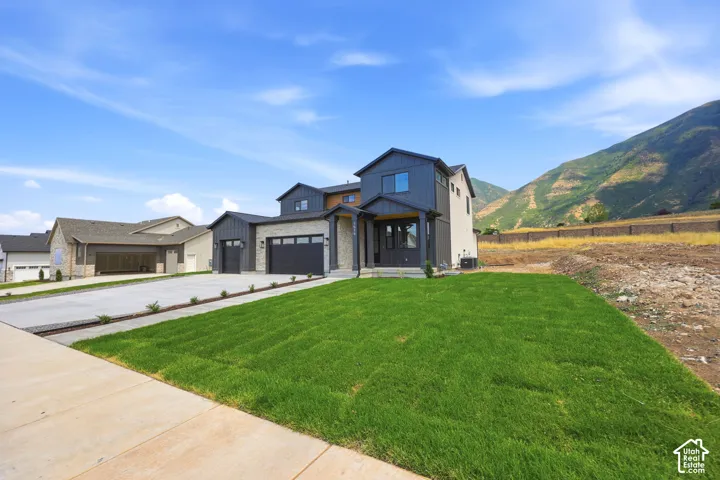 Modern dwelling featuring a stone and dark siding exterior, an attached two-car garage, a covered entryway, a manicured front lawn, and a concrete driveway