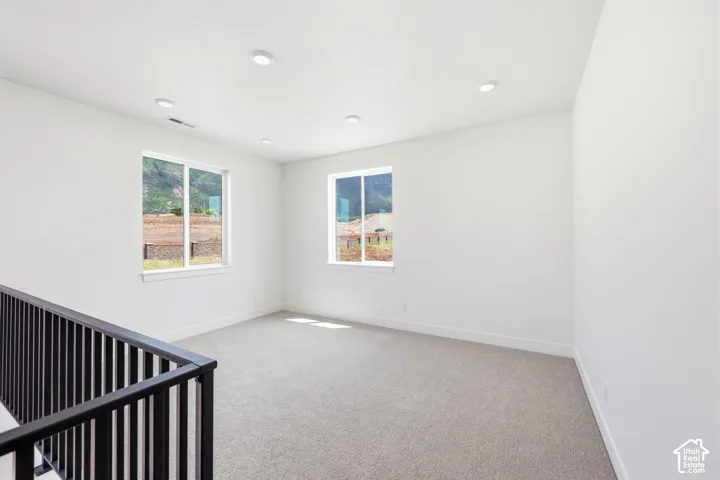 Carpeted upstairs landing featuring a black metal railing, recessed ceiling lighting, two windows, and white baseboards