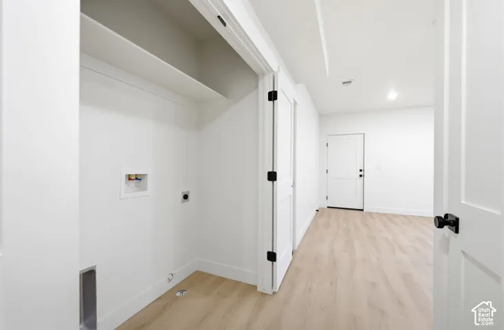 Dedicated laundry area with hookups, built-in shelving, light wood-finish flooring, white walls, and contemporary black hardware