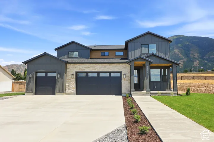 Modern exterior featuring dark vertical siding, stone accents, a covered entry, a three-car garage, and a concrete driveway