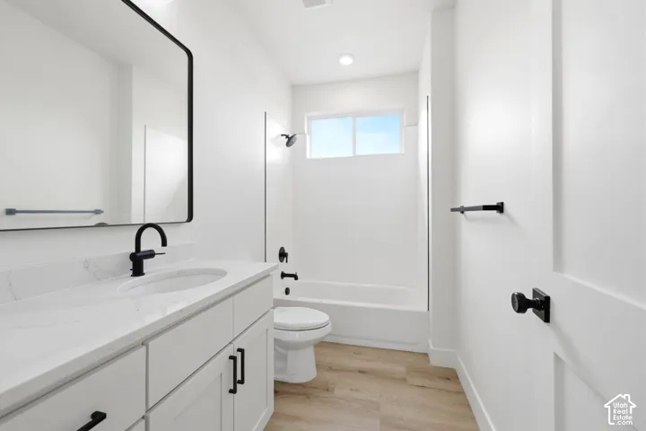 Bathroom featuring a rectangular mirror with a black frame, a white vanity with a single basin, a white countertop with subtle veining, matte black hardware, and wood-finish flooring