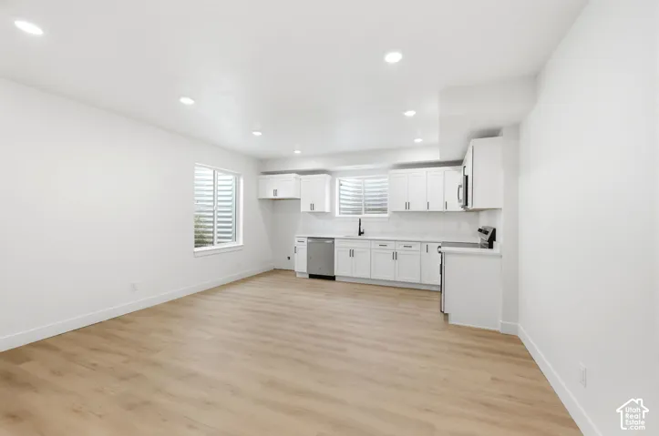 Open-concept living space featuring wood-finish flooring, recessed lighting, and a kitchen with white cabinetry, stainless steel appliances, and a black faucet