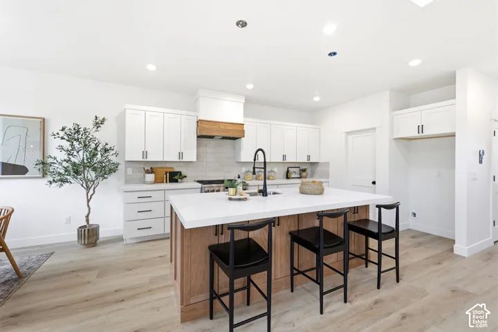 Contemporary kitchen featuring a large central island with seating, white shaker-style cabinetry, and light wood-finish flooring