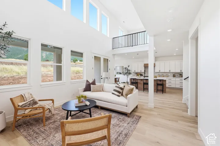 Bright open-concept living area featuring a two-story ceiling with high windows, light wood-finish flooring, and an open balcony overlooking the space
