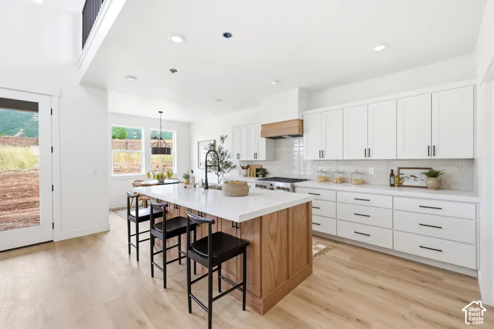 Open-concept kitchen featuring an oversized island with seating, a gas range, white cabinetry, a tiled backsplash, and wood-finish flooring