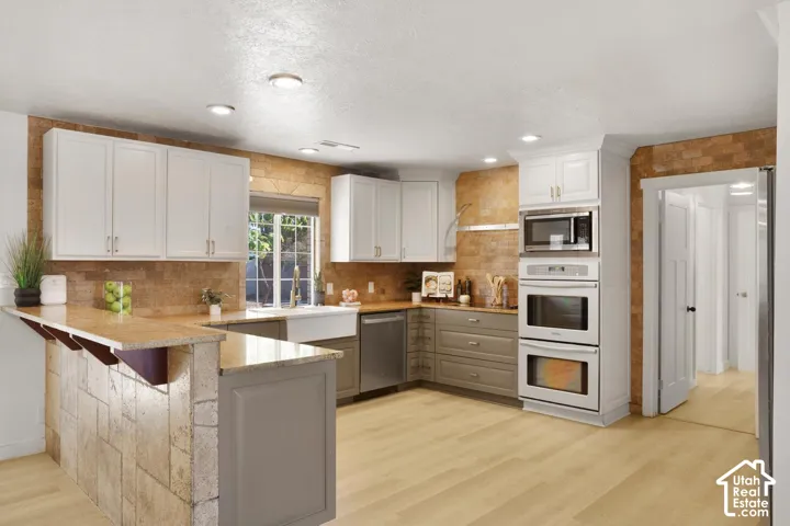 Kitchen featuring light wood-finish flooring, white upper cabinetry, gray lower cabinetry, a built-in double oven, and a tiled backsplash