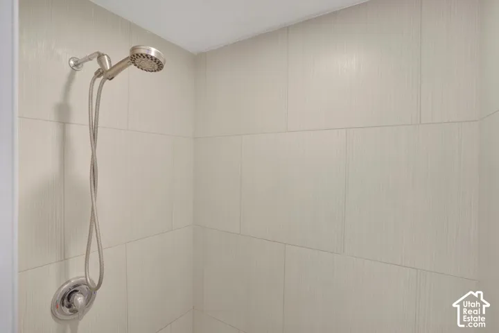 Shower with light-toned rectangular tile surround and a brushed nickel shower head with handheld attachment